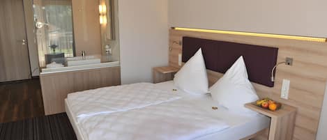A hotel room with a bed, a nightstand, a mirror, and a small table with fruits.