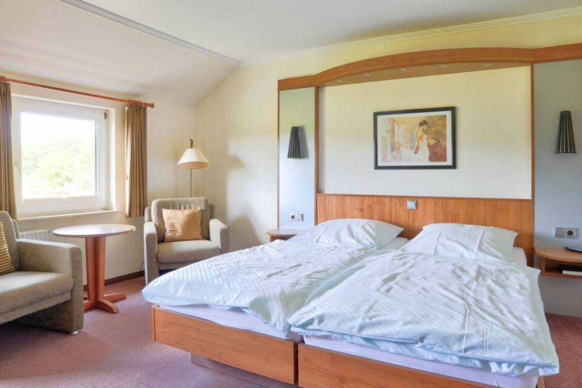 Una camera d'albergo con un letto, due poltrone, un tavolino e una lampada.