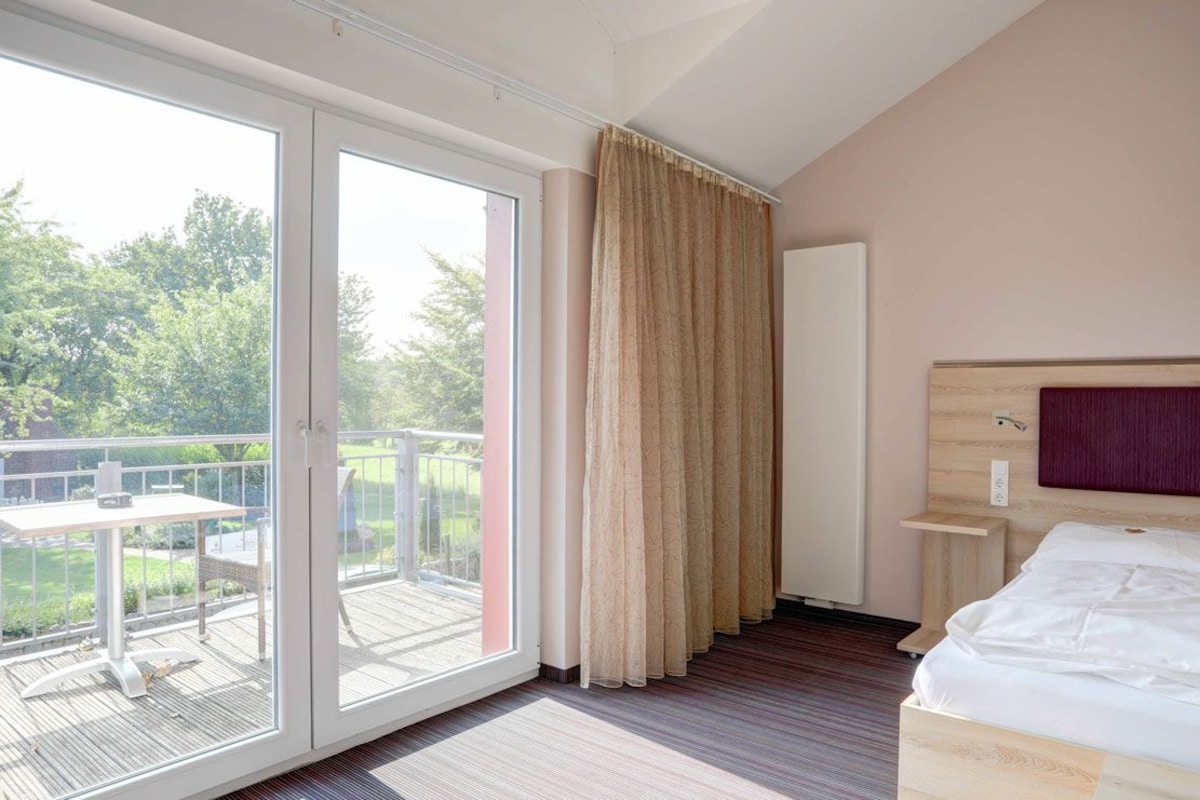 A single room with a balcony, a bed, a bedside table, and a headboard.