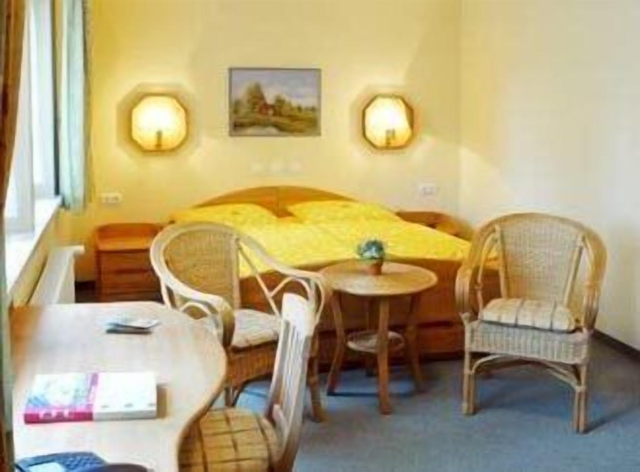 Een kamer met een bed, twee wandlampen, een ronde tafel met stoelen en een raam met gordijnen.