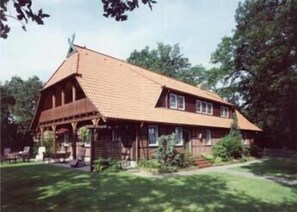A traditional wooden house with a gabled roof, a porch with wooden railings, and a well-maintained lawn. - Stössel's Hotel & Restaurant (Altenmedingen)