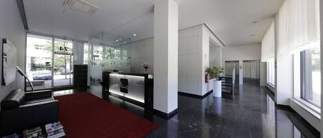 Eine moderne Hotellobby mit einer Rezeption, einem roten Teppich und einem großen Fenster mit Blick auf die Straße.
