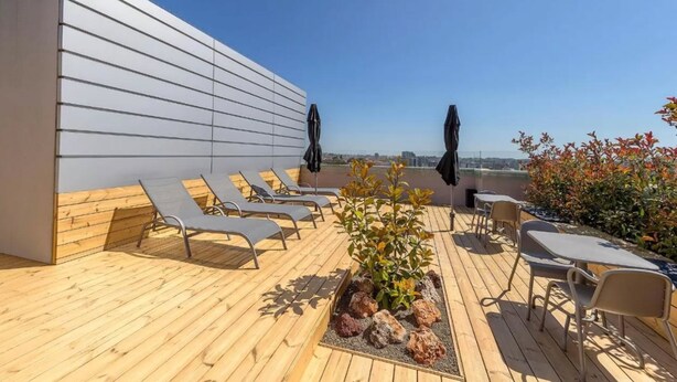 Una terraza en la azotea con piso de madera, sillones y mesas.