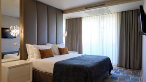 Una habitación de hotel con una cama grande, una mesita de noche, un televisor y una ventana con cortinas.