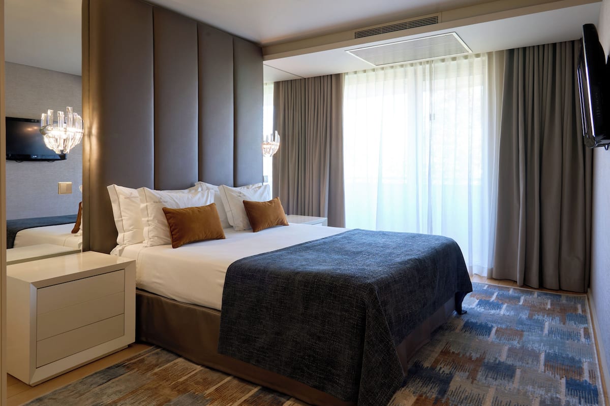 A hotel room with a large bed, a bedside table, a TV, and a window with curtains.