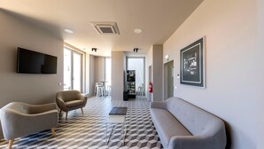 Un vestíbulo moderno con piso a cuadros, un sofá, dos sillones, un televisor de pantalla plana y una máquina expendedora.