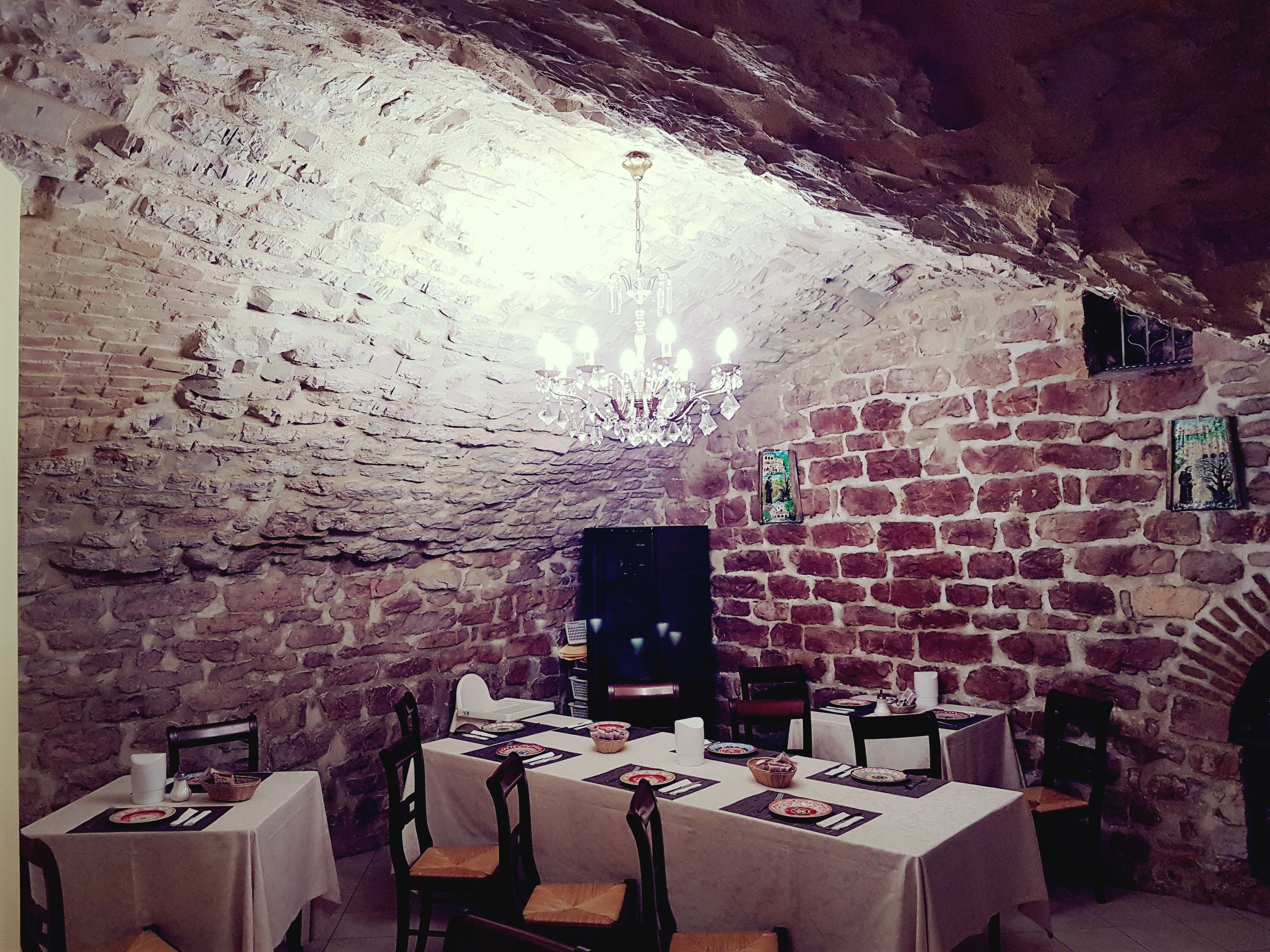 A rustic dining area with exposed brick walls, a chandelier, and tables set for a meal. - Hotel Ponte San Vittorino (Assisi)