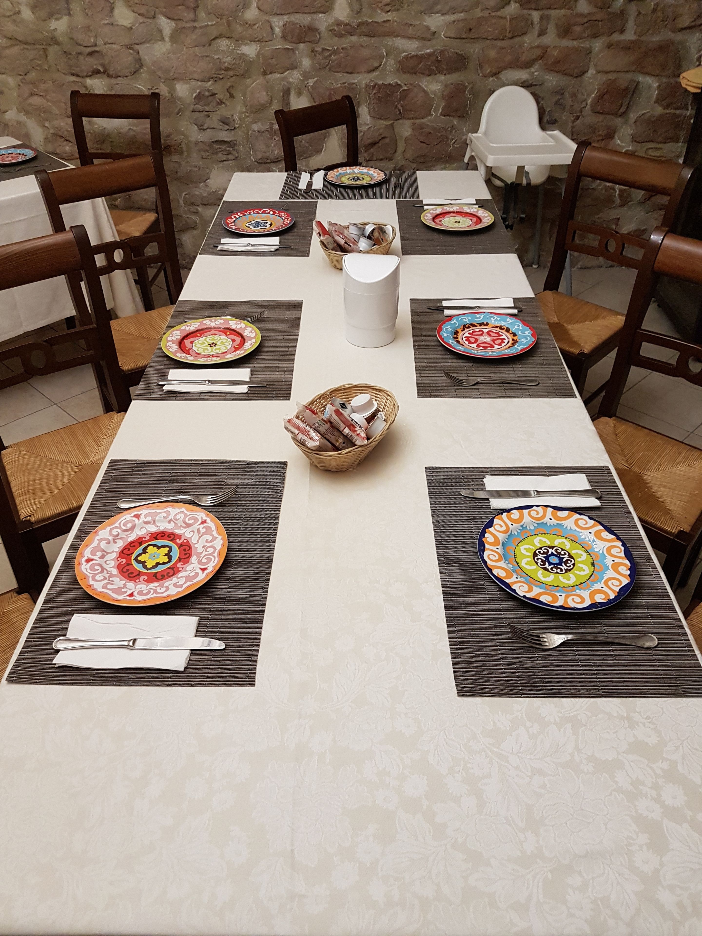 A dining table set with colorful plates, a white pitcher, and wicker baskets.