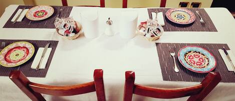 A dining table set for six with a white tablecloth, wooden chairs, and colorful plates.