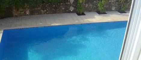 A clear blue swimming pool with a tiled deck and a stone wall in the background.