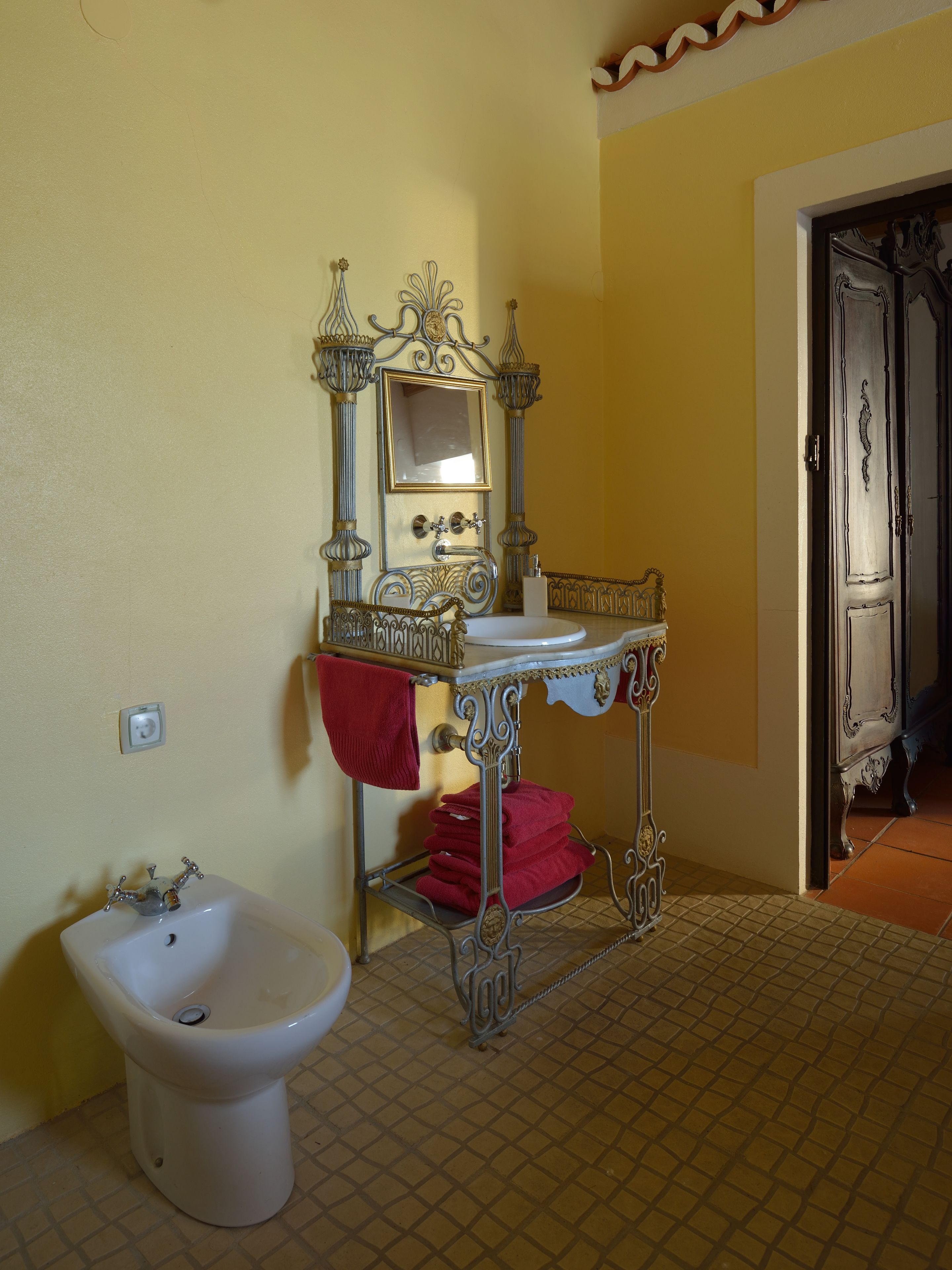 Ein Badezimmer mit einem weißen Waschbecken, einem Bidet und einem Spiegel mit aufwendiger Metallverzierung.