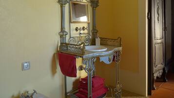 Une salle de bain avec un lavabo blanc, un bidet et un miroir orné de motifs métalliques.