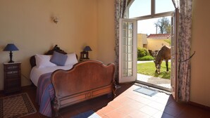 A bedroom with a wooden bed, two bedside tables with lamps, a large window, and a view of a horse outside. - Quinta do Scoto (Sintra)