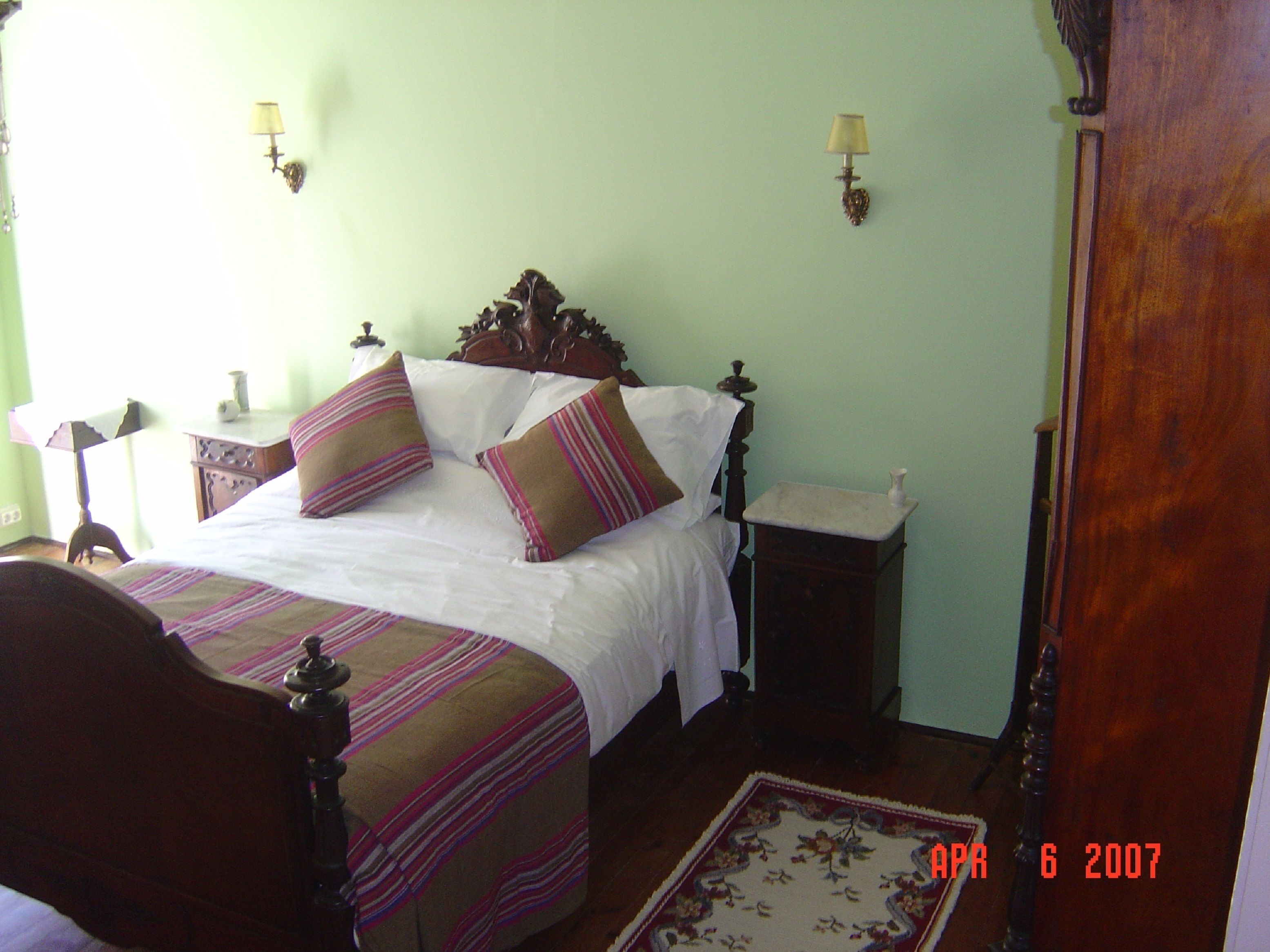 A bedroom with a wooden bed, two bedside tables, a nightstand, a night lamp, and a floral rug.