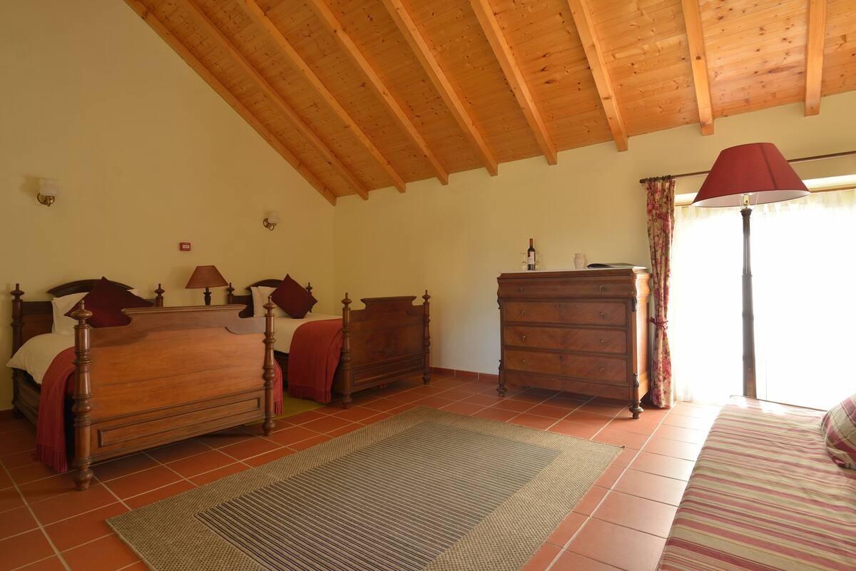 A bedroom with a wooden ceiling, a bed with a red headboard, a dresser, and a lamp.