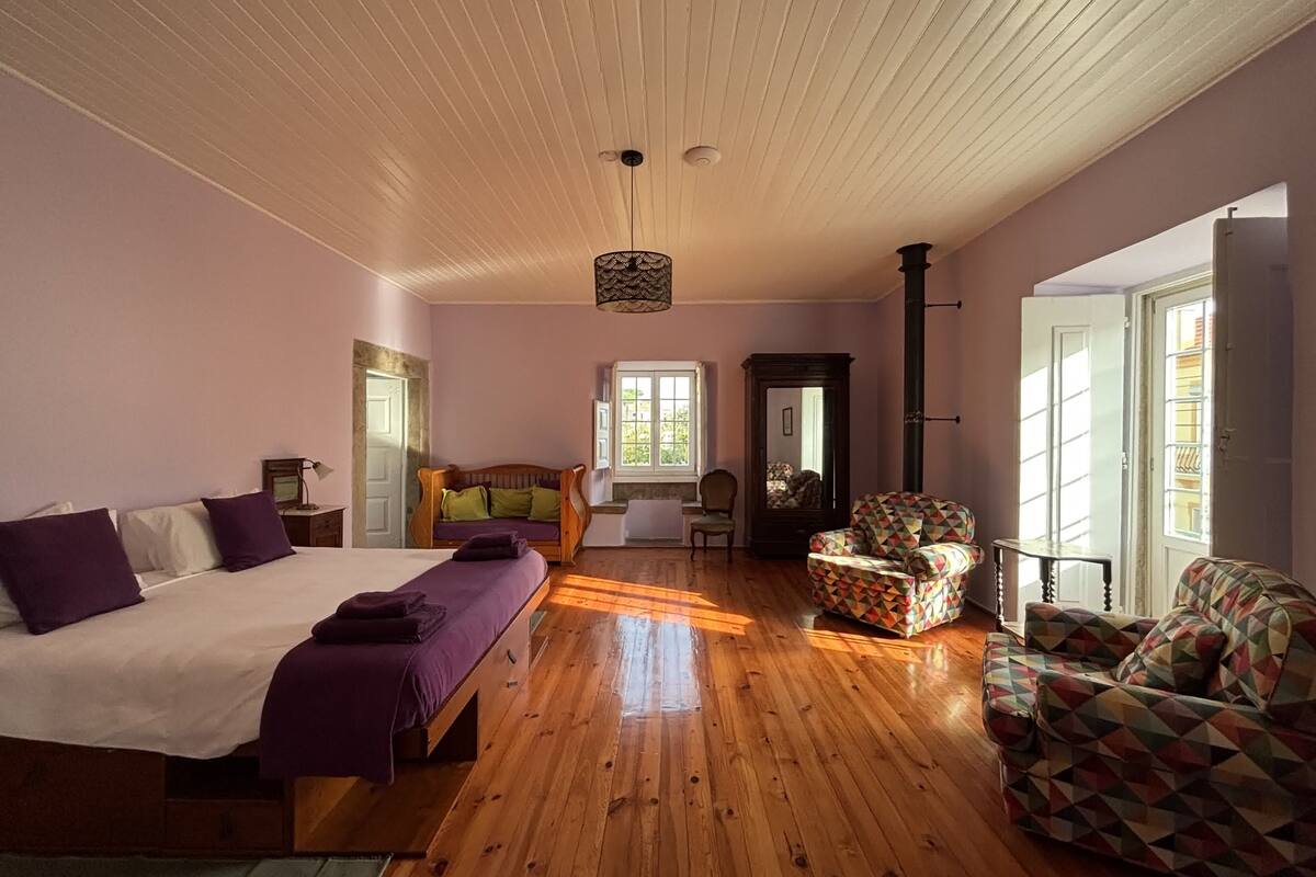 A bedroom with a bed, a wooden floor, a sofa, a chair, and a mirror.