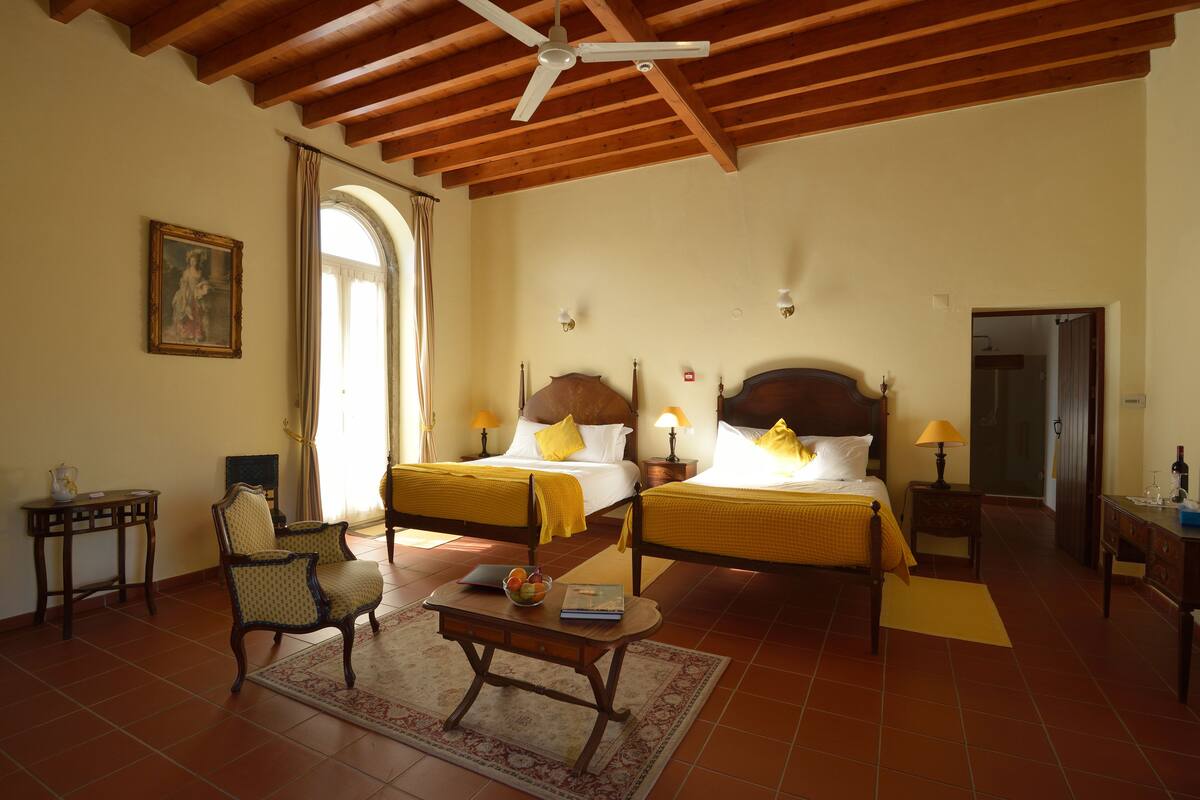 A hotel room with two beds, wooden furniture, a ceiling fan, and a painting on the wall.