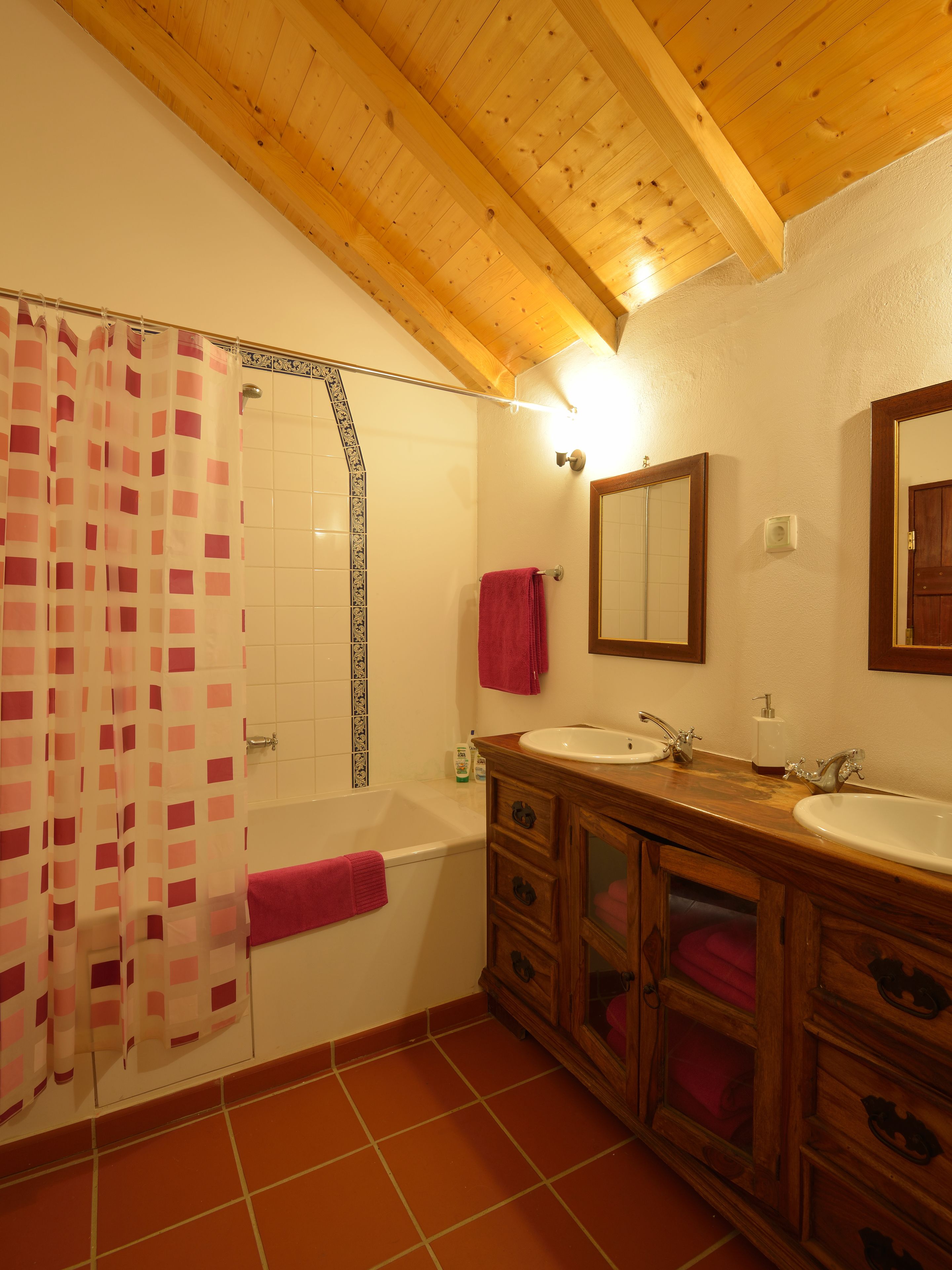 A bathroom with wooden beams, a bathtub, two sinks, a mirror, and a shower curtain.