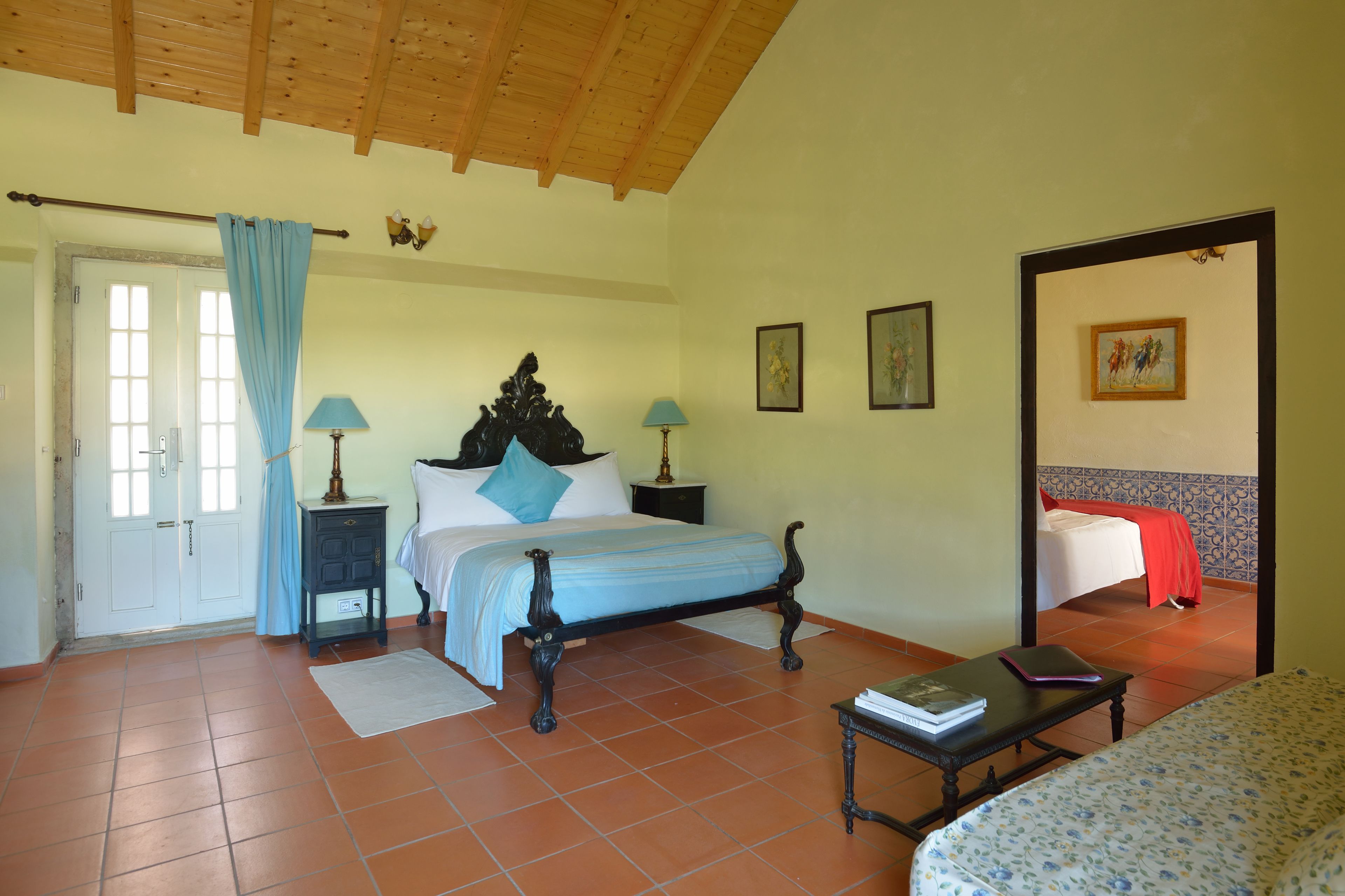Une chambre à coucher avec un lit, des tables de chevet, une commode, une porte et une fenêtre avec des rideaux.