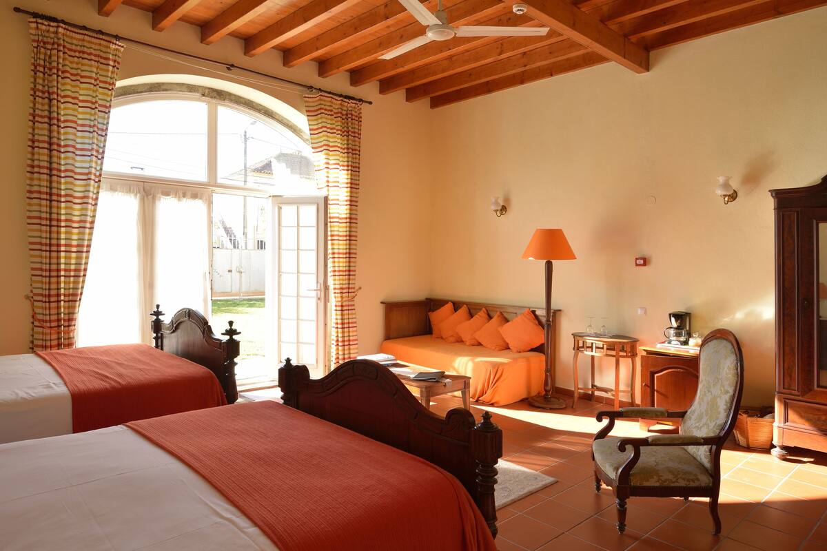 A bedroom with two beds, a sofa, a chair, a desk, and a lamp.