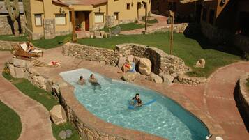 A swimming pool surrounded by stone walls and a patio area with a few people.
