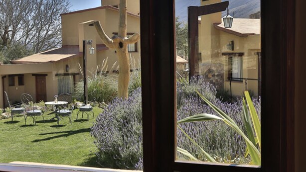 A view of a courtyard with outdoor seating, a wooden sculpture, and a building with a mountain backdrop. - Hotel El Reposo del Diablo (Tilcara)