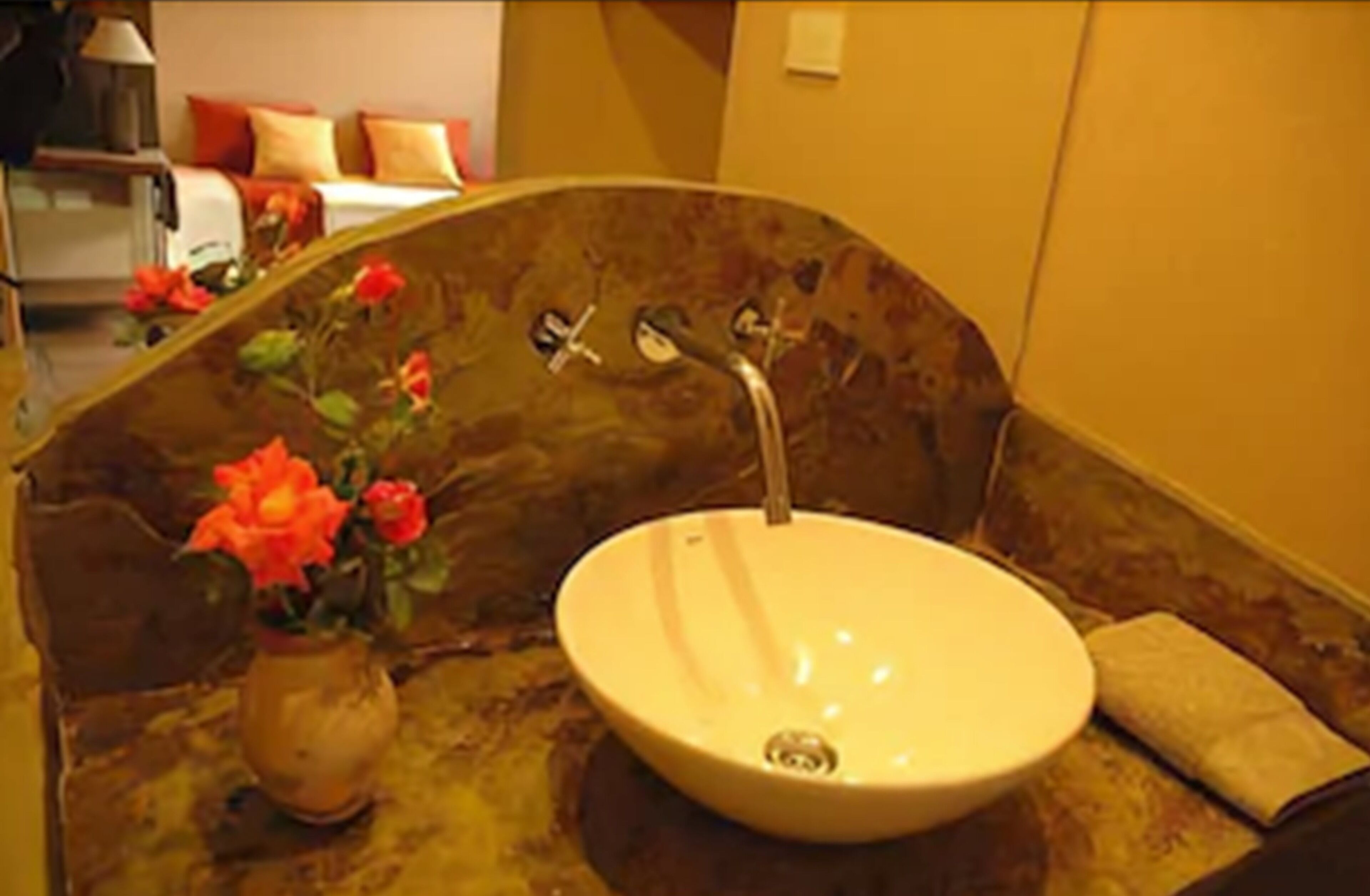 A bathroom with a round sink, a vase with flowers, and a towel on a wooden surface.