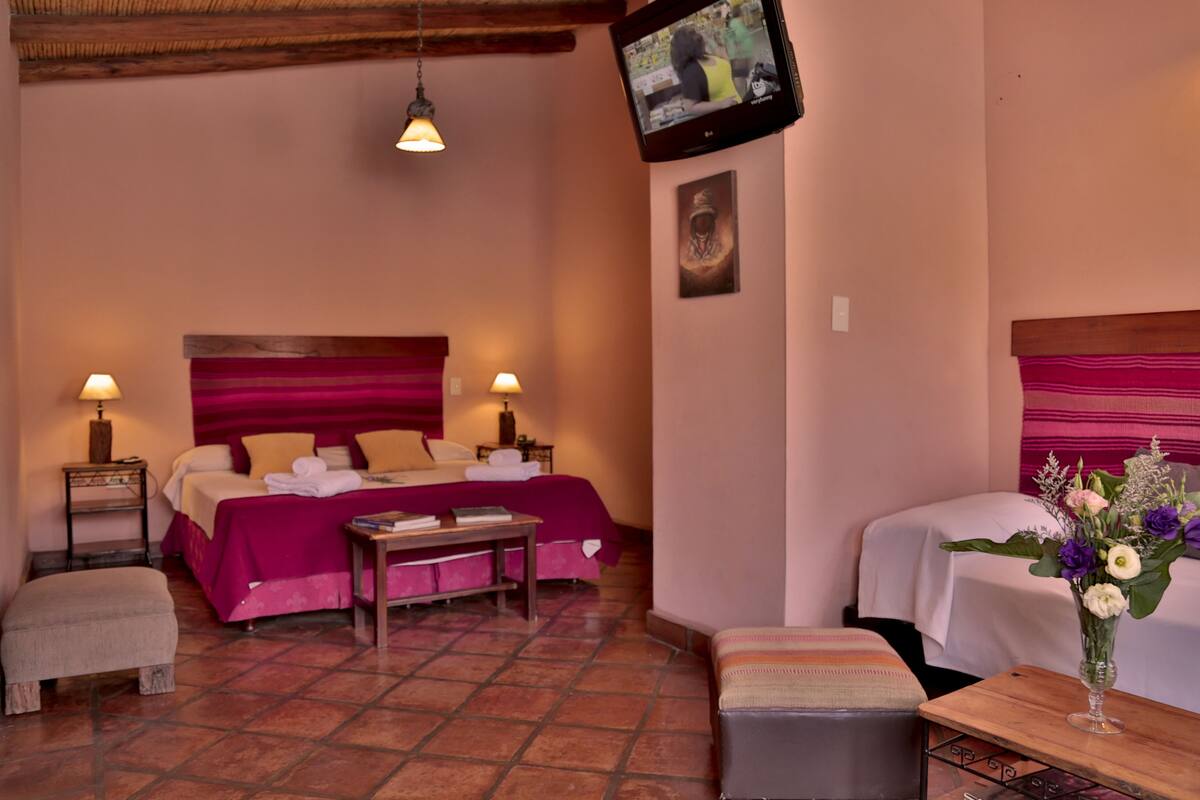 A hotel room with a bed, bedside tables, a TV, a small table with a vase of flowers, and a bench.
