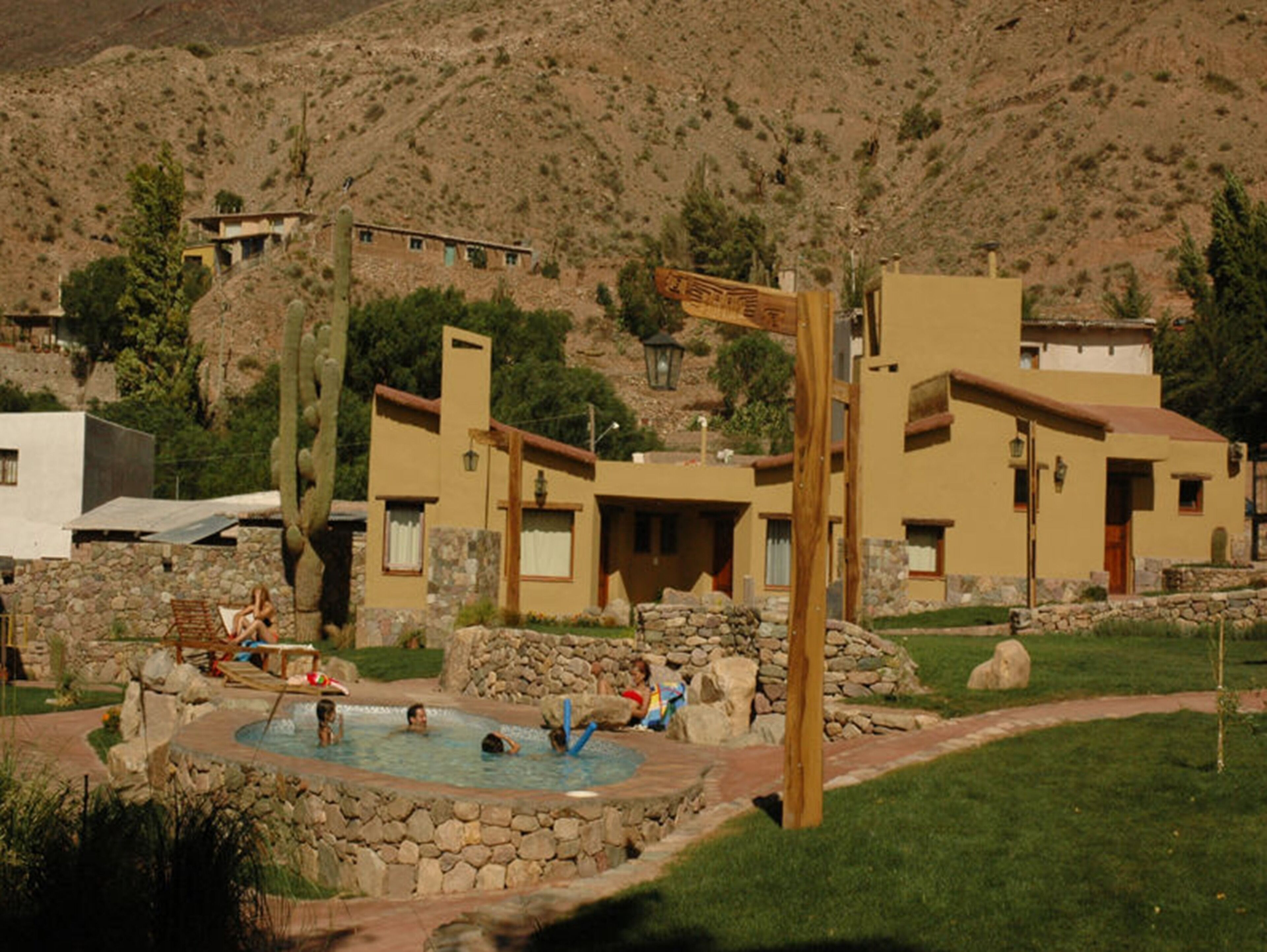 A pool area with stone walls and a wooden signpost, surrounded by buildings with a desert-style architecture.