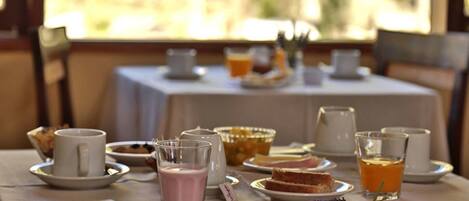 A breakfast table set with plates, glasses, and a coffee pot, with a view of greenery outside.