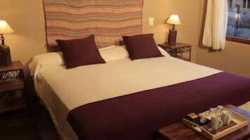 Una cama bien hecha con dos almohadas, un cabecero de madera, lámparas de noche y una bandeja con una taza y un libro sobre una mesita de noche de madera.