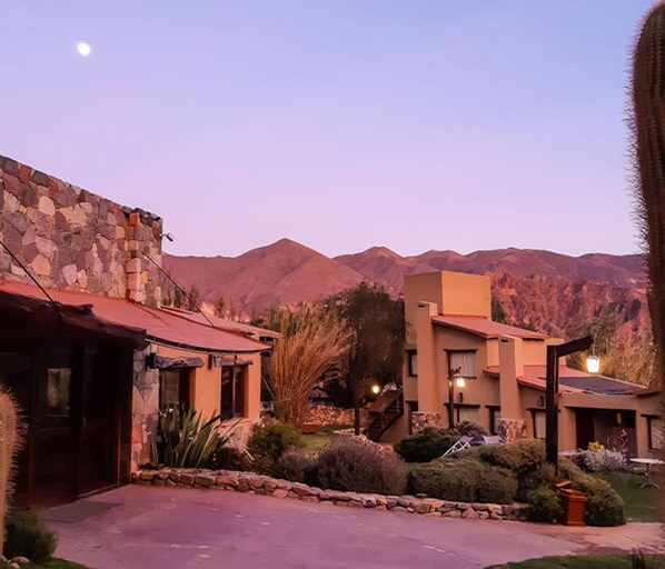 A building with a stone facade and a red roof, surrounded by landscaped gardens and a mountain backdrop. - Hotel El Reposo del Diablo (Tilcara)