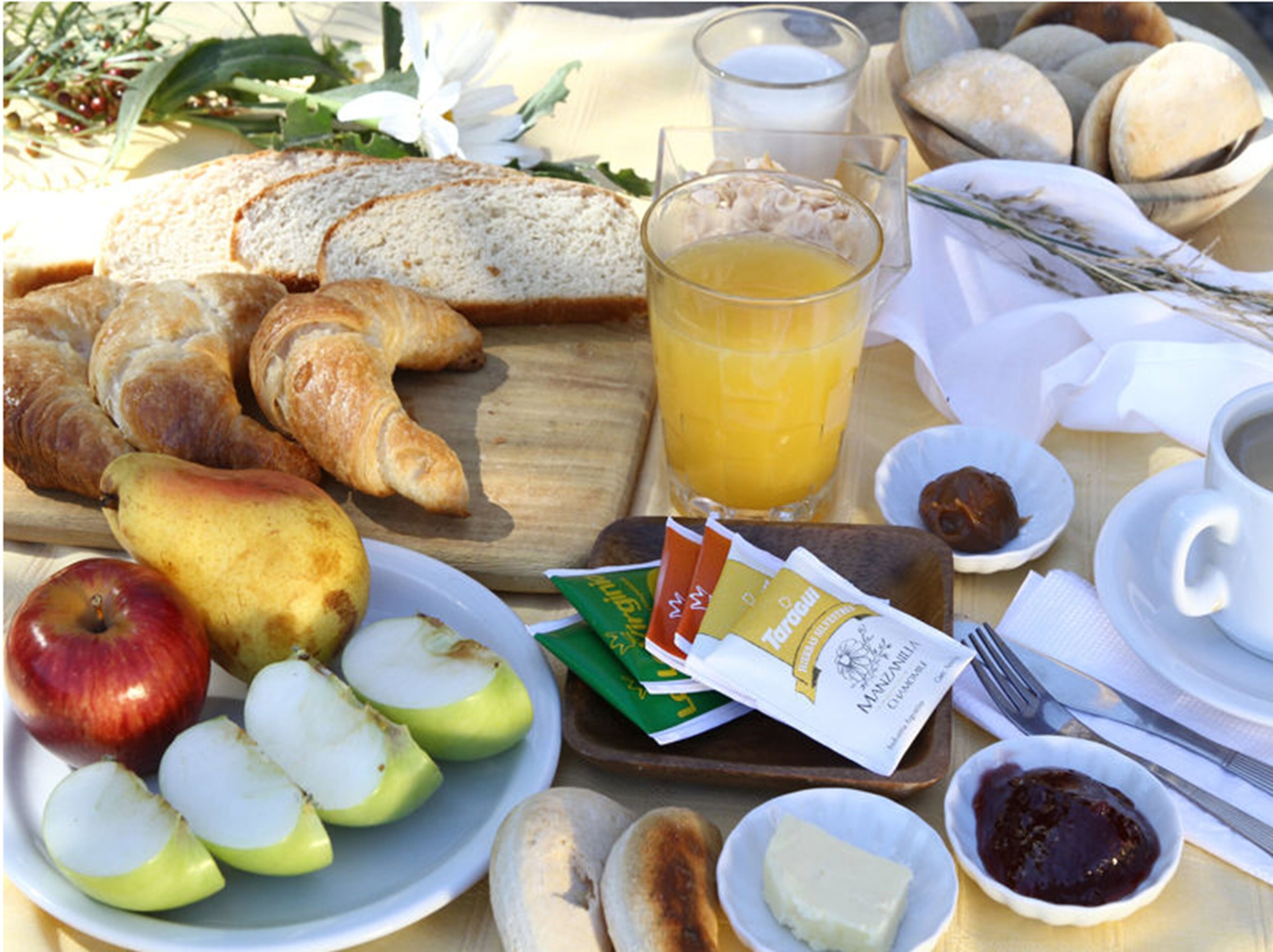 Una mesa de desayuno con cruasanes, pan, manzanas, jugo y salsas.