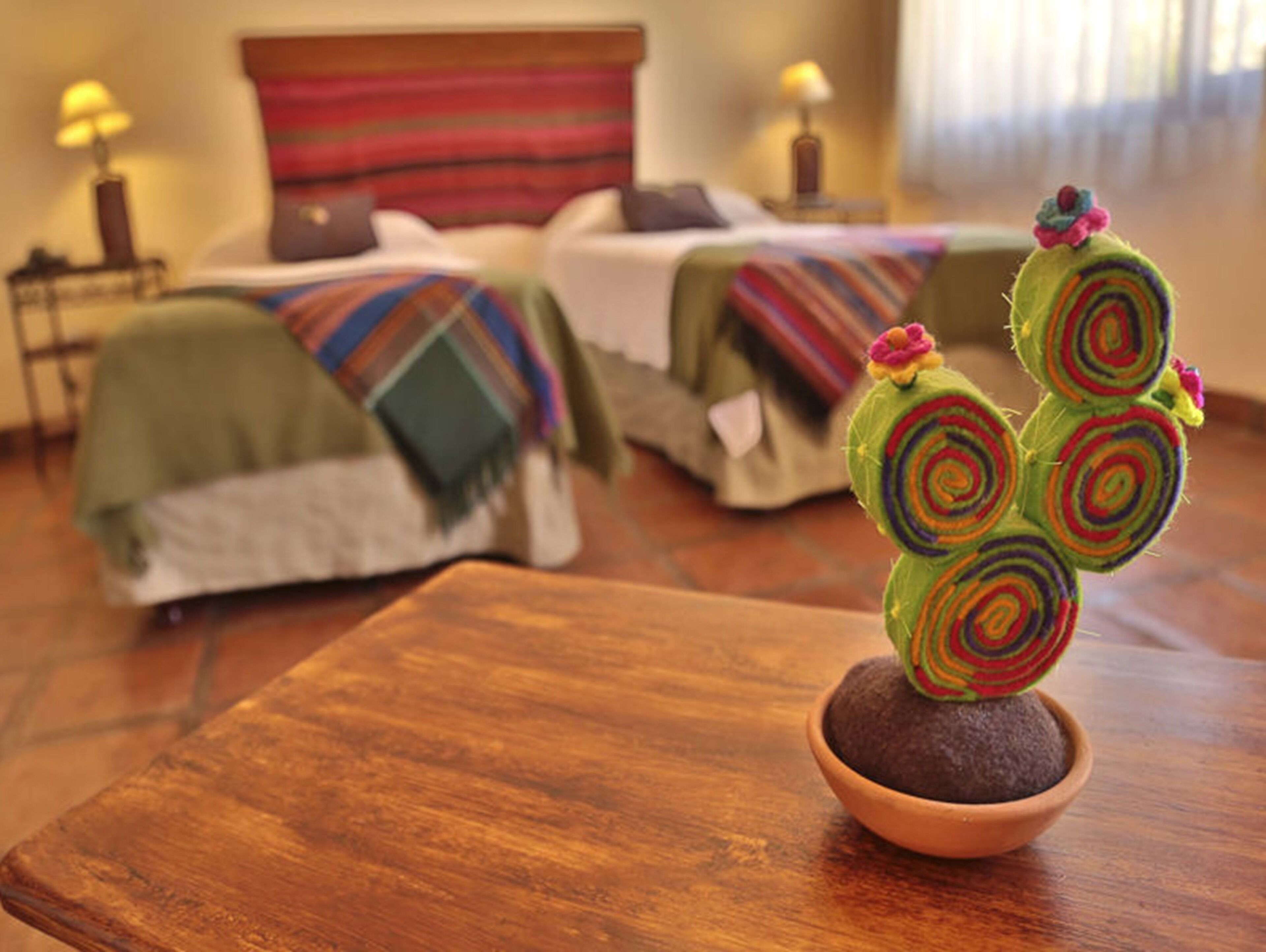 Una habitación con una cama, una mesita con un cactus y una lámpara.