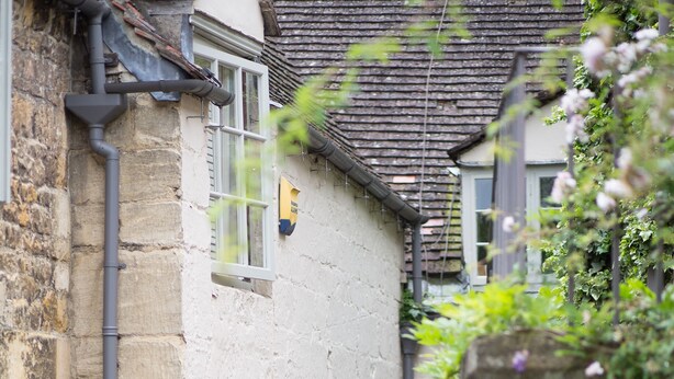 A narrow stone pathway between buildings with a small potted plant and a metal sign on the wall. - The Lion Inn (Cheltenham)