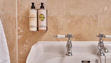 Ein Badezimmer mit einer Badewanne, zwei Flaschen Bramble Handcreme und einem historischen Waschbecken.