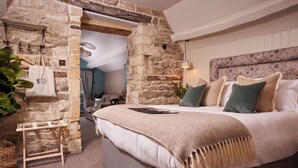 A bedroom with a stone wall, a bed with a beige blanket, and a hanging plant. - The Lion Inn (Cheltenham)
