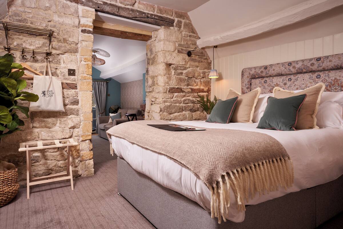 A bedroom with a stone wall, a bed with a beige blanket, and a hanging plant.