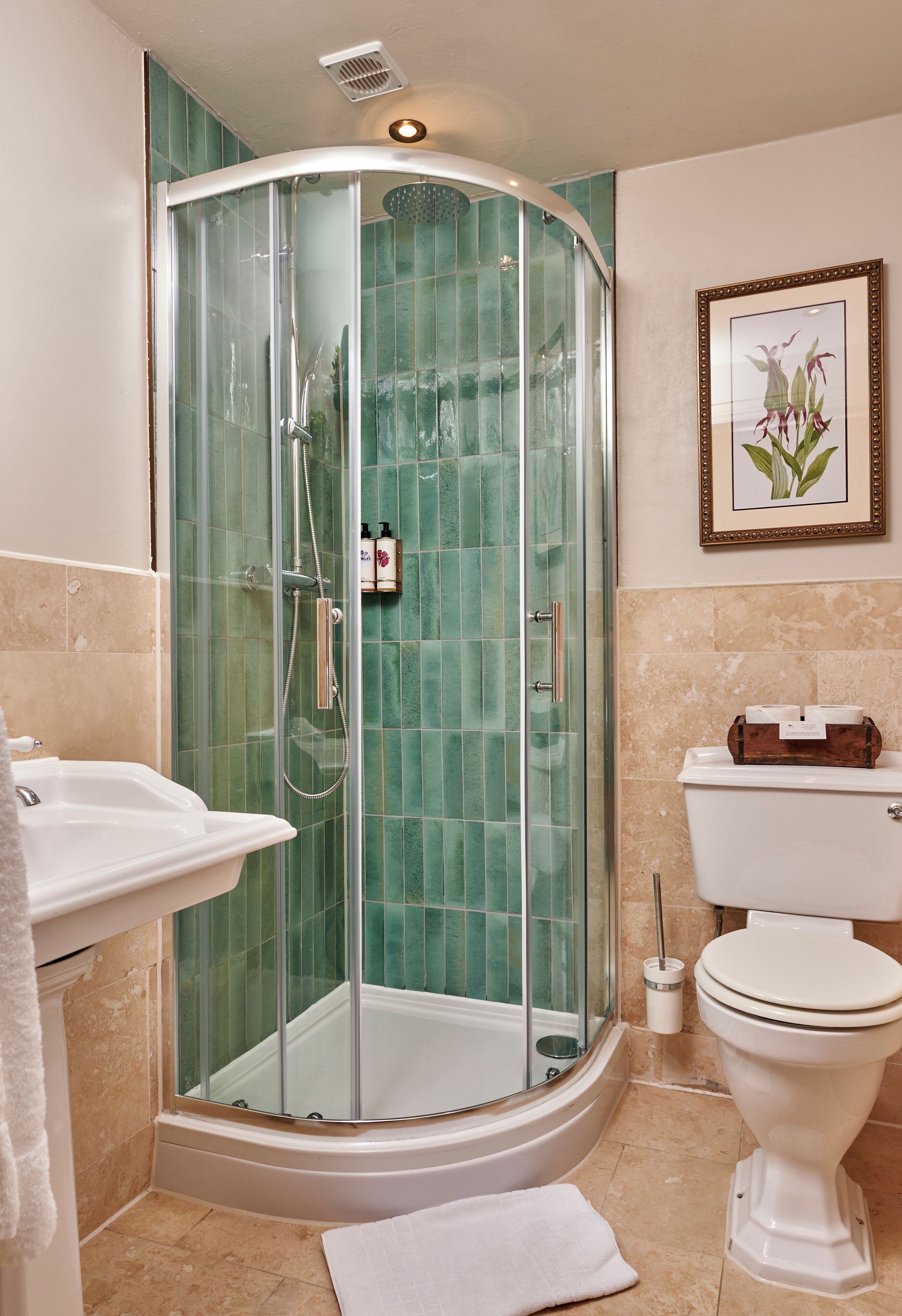 A bathroom with a glass-enclosed shower, a white sink, a toilet, and a framed picture on the wall.