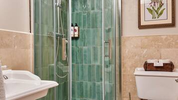 A bathroom with a glass-enclosed shower, a white sink, a toilet, and a framed picture on the wall.