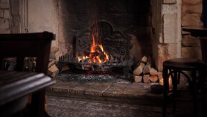 A fireplace with burning logs, a stone wall, and a wooden chair. - The Lion Inn (Cheltenham)
