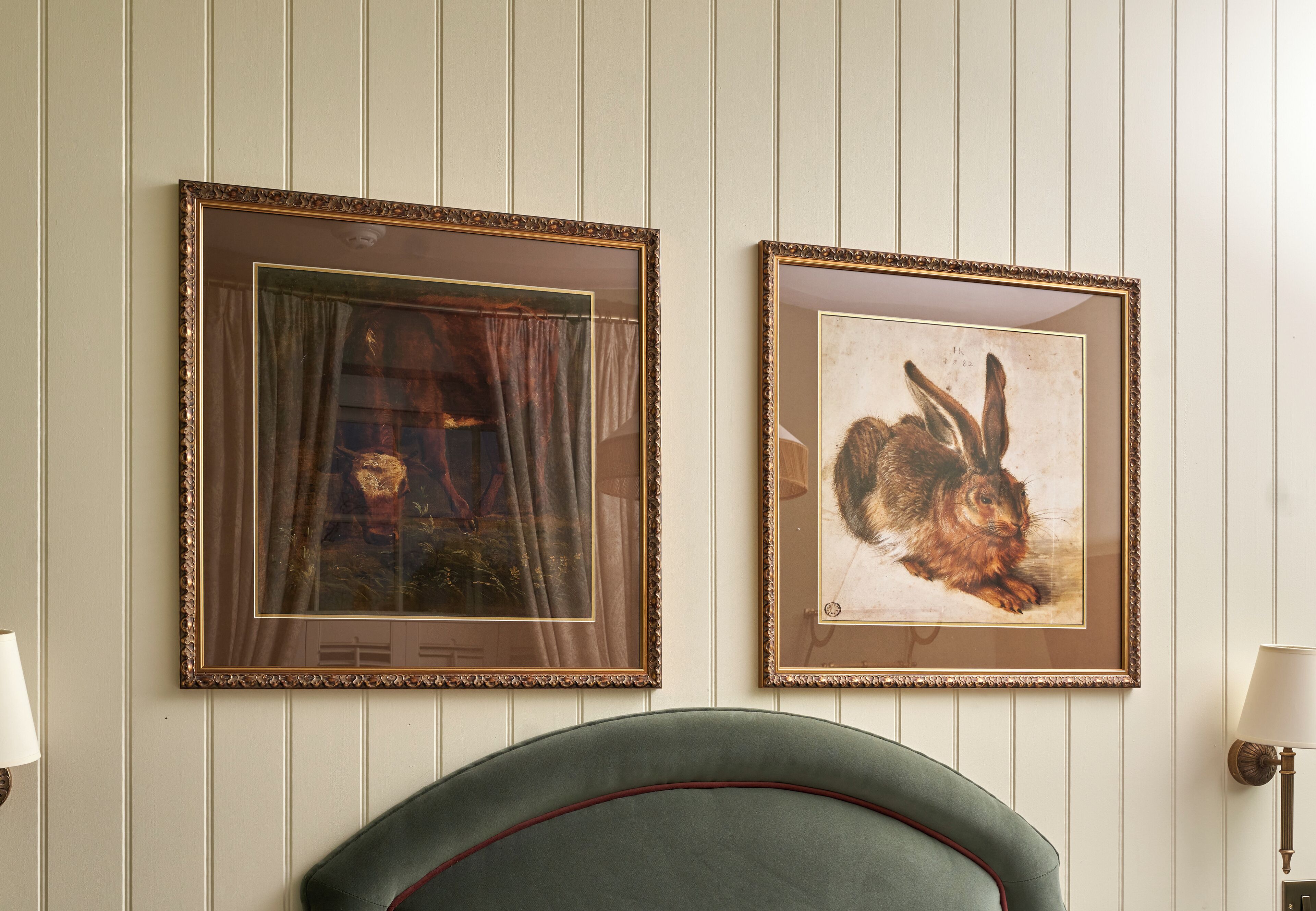 Two framed artworks on a wall, a curtain, and a green upholstered chair.