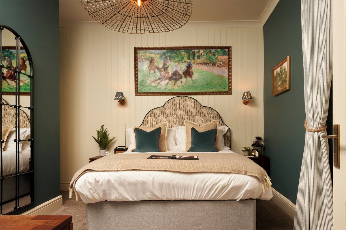 A bedroom with a large bed, a headboard, a hanging light fixture, and a painting on the wall.