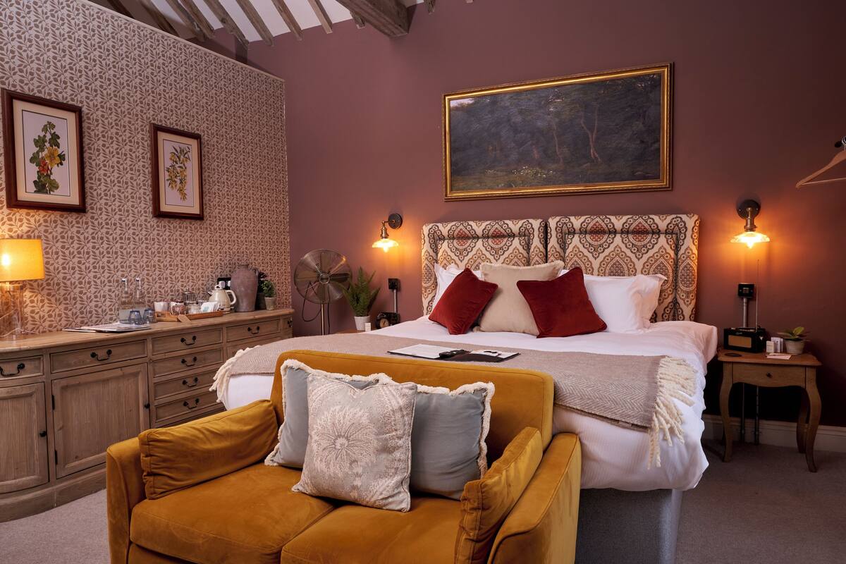 A bedroom with a large bed, a wooden dresser, a sofa, and a painting on the wall.