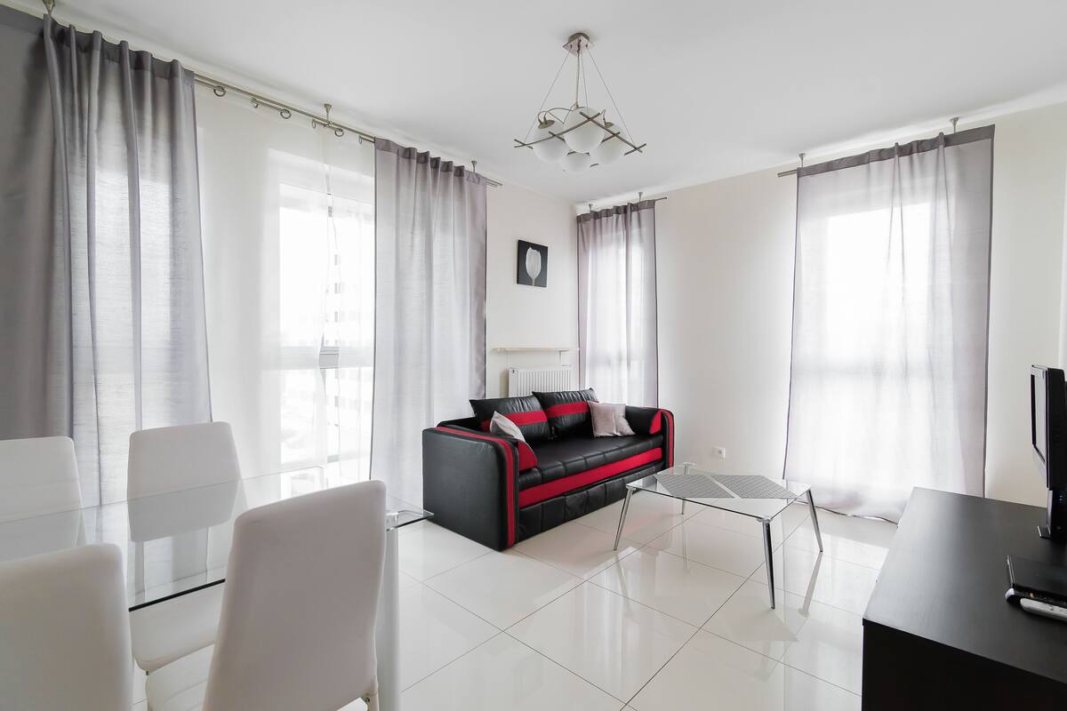A modern living room with a black and red sofa, a glass coffee table, and a TV on a black stand.