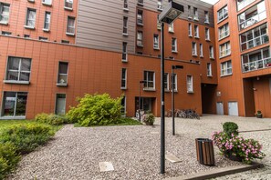 A multi-story building with a red brick facade, multiple windows, and a gravel courtyard with greenery and a trash bin. - Senator Warsaw Apartments (Warsaw)