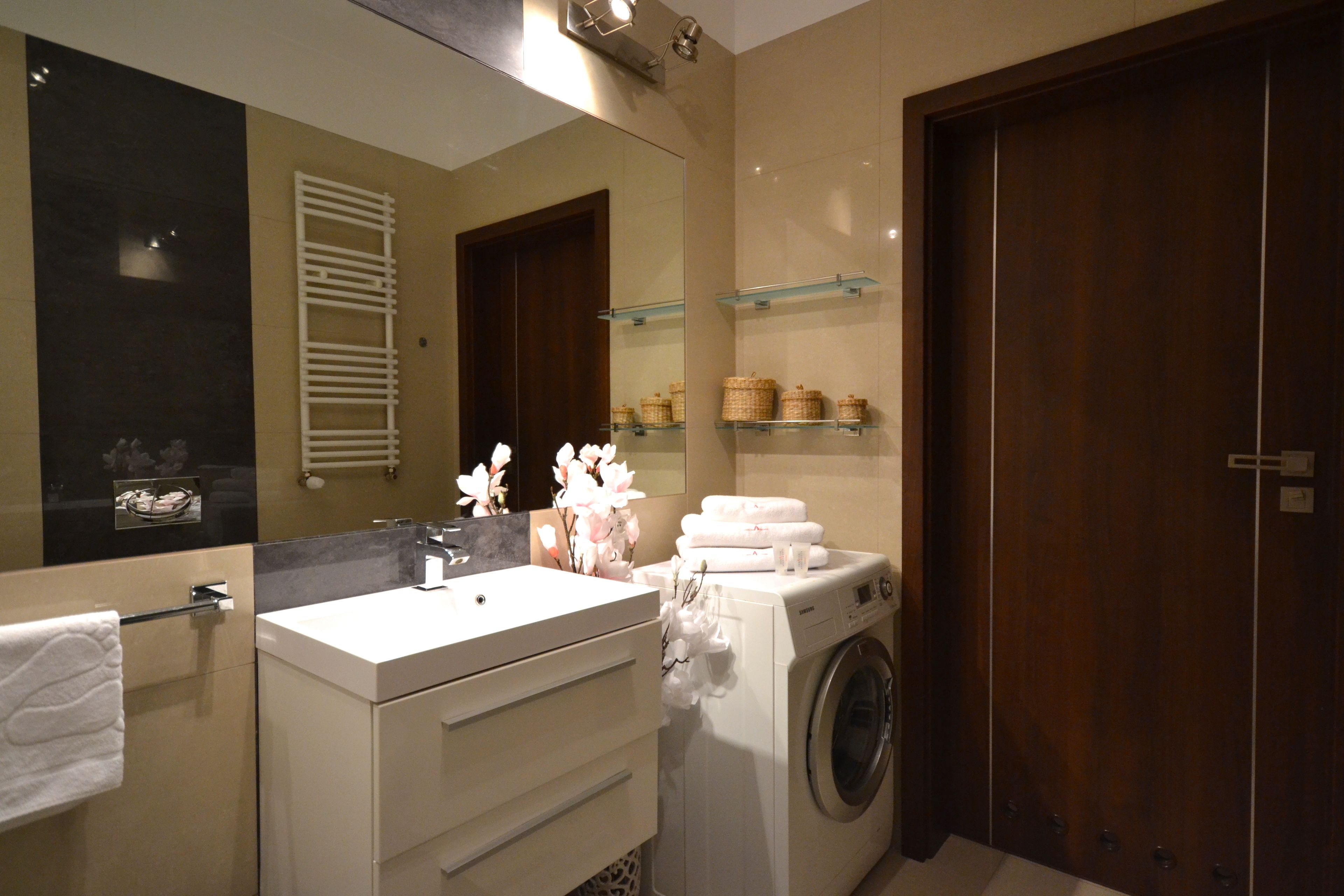 Un baño moderno con un lavamanos blanco, un espejo, una lavadora y una puerta de madera.