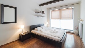 A bedroom with a bed, bedside lamps, a mirror, shelves, and a window with blinds. - Senator Warsaw Apartments (Warsaw)