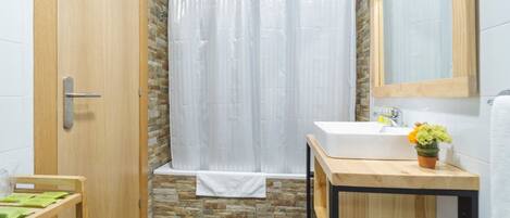 Un baño con puerta de madera, cortina de ducha, lavamanos, espejo y una pequeña mesa con una planta.
