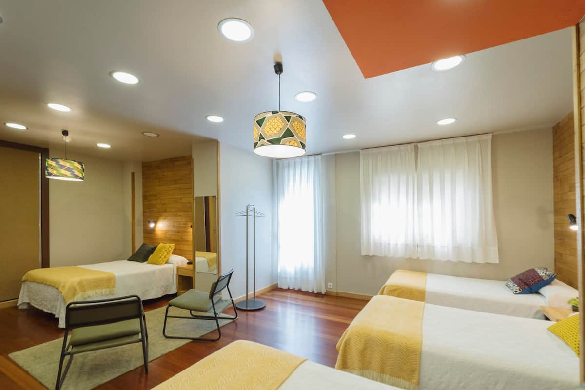 Quarto de hotel com duas camas de solteiro, uma cadeira, luminária pendente e espelho.